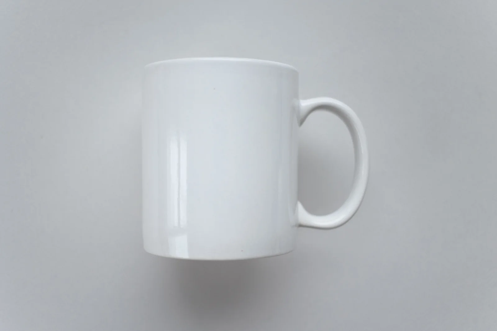 Taza blanca física sin impresión sobre una superficie gris clara.